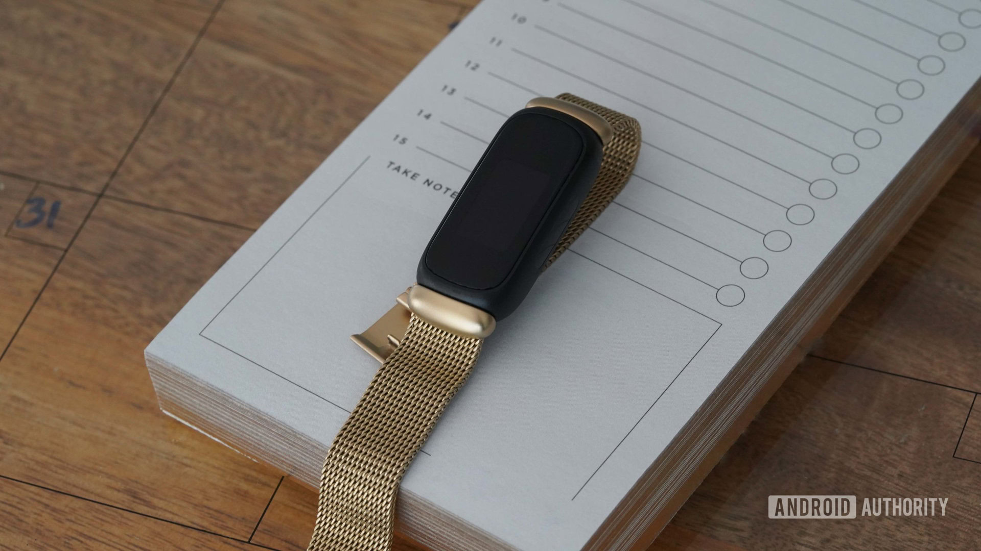 Fitbit Inspire 3 Stainless Steel Band A Fitbit Inspire 3 with a gold stainless steel mesh band rests on a notepad.